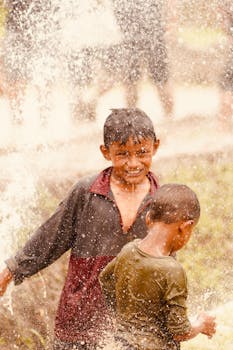 Two children joyfully playing in a water splash, outdoors in a rural setting.